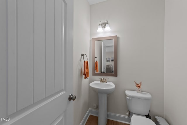 half bathroom featuring toilet, baseboards, and a sink