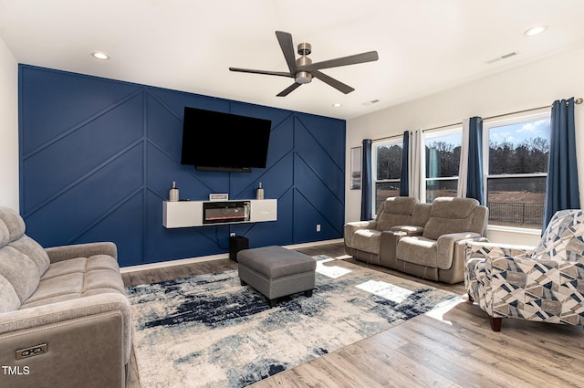 living room with visible vents, recessed lighting, wood finished floors, a decorative wall, and a ceiling fan