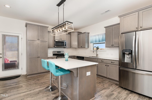 kitchen with visible vents, a kitchen island, a sink, light wood-style floors, and appliances with stainless steel finishes