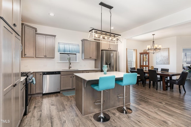 kitchen featuring a breakfast bar area, wood finished floors, a sink, stainless steel appliances, and a notable chandelier