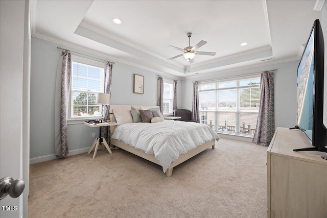 bedroom with a tray ceiling, multiple windows, and light colored carpet