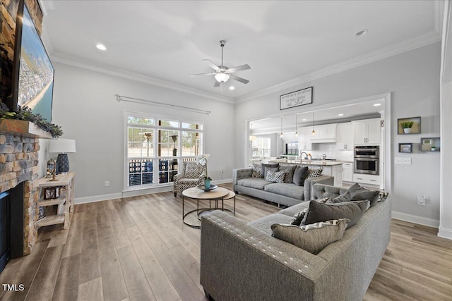 living room featuring light wood-type flooring, a fireplace, baseboards, and crown molding