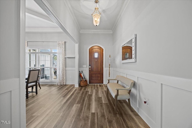 foyer featuring arched walkways, a decorative wall, a wainscoted wall, wood finished floors, and ornamental molding