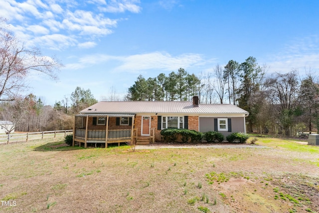 ranch-style home with brick siding, a chimney, metal roof, fence, and a front yard