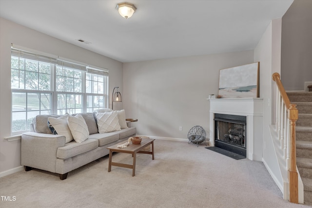 carpeted living room with stairway, a fireplace with flush hearth, visible vents, and a healthy amount of sunlight