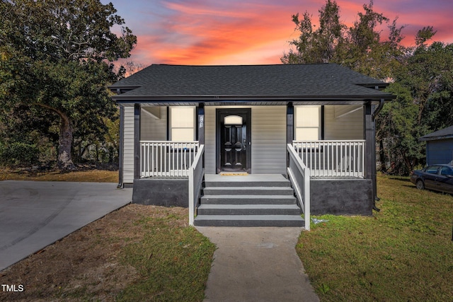 bungalow featuring a yard, a porch, and a shingled roof