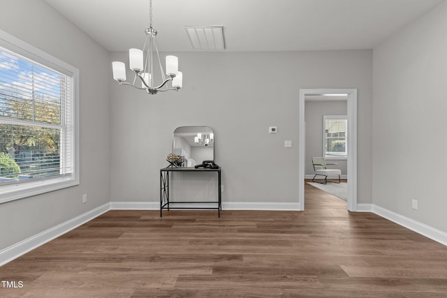 unfurnished dining area with a wealth of natural light, visible vents, a notable chandelier, and wood finished floors