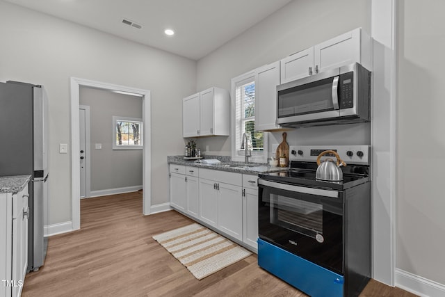 kitchen with white cabinets, light wood-style flooring, light stone counters, appliances with stainless steel finishes, and a sink