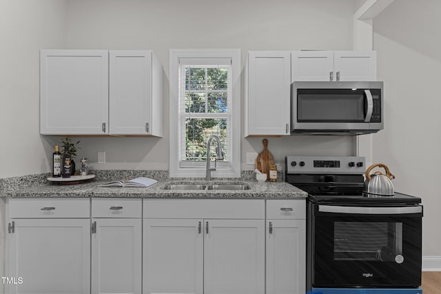 kitchen with stainless steel microwave, electric range, white cabinetry, a sink, and light stone countertops