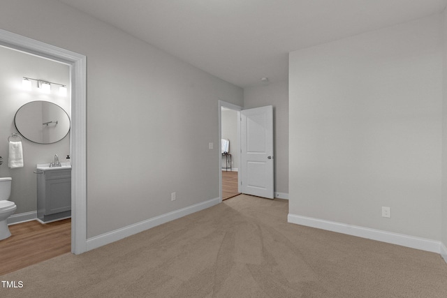 unfurnished bedroom featuring light colored carpet, a sink, ensuite bath, and baseboards