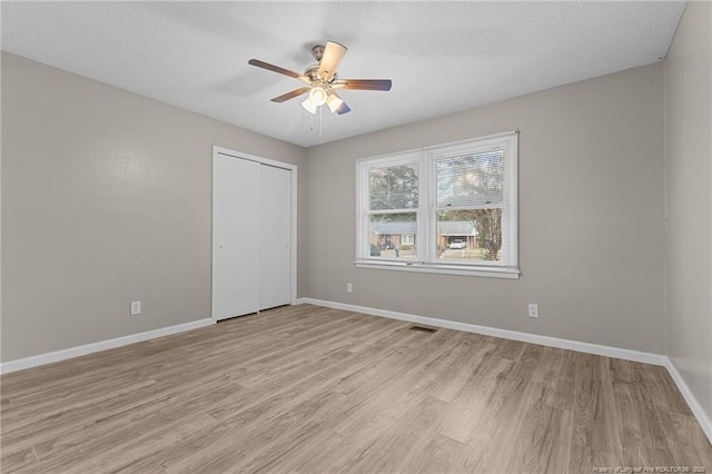 empty room featuring light wood finished floors, baseboards, visible vents, and ceiling fan