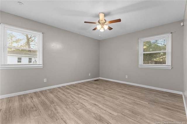 spare room with light wood-type flooring, ceiling fan, visible vents, and baseboards