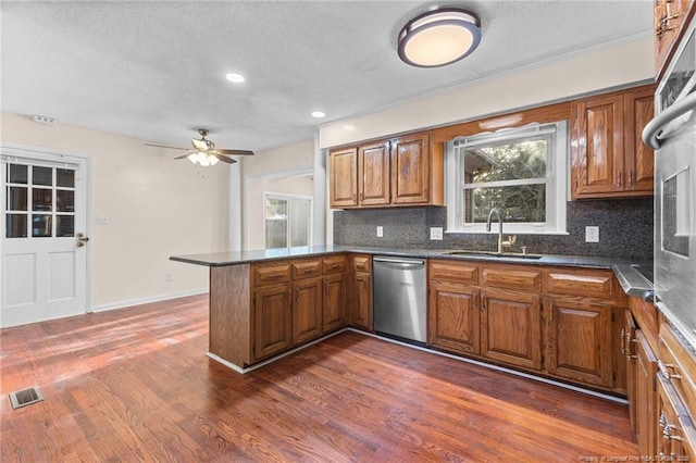 kitchen featuring visible vents, stainless steel dishwasher, brown cabinetry, a sink, and a peninsula