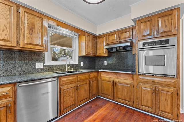 kitchen featuring under cabinet range hood, a sink, ornamental molding, appliances with stainless steel finishes, and brown cabinets