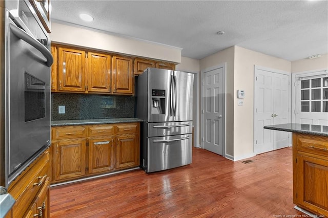 kitchen with tasteful backsplash, brown cabinetry, dark wood finished floors, appliances with stainless steel finishes, and a textured ceiling