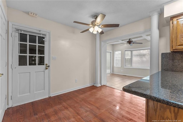 unfurnished dining area featuring baseboards, ceiling fan, ornate columns, and wood finished floors