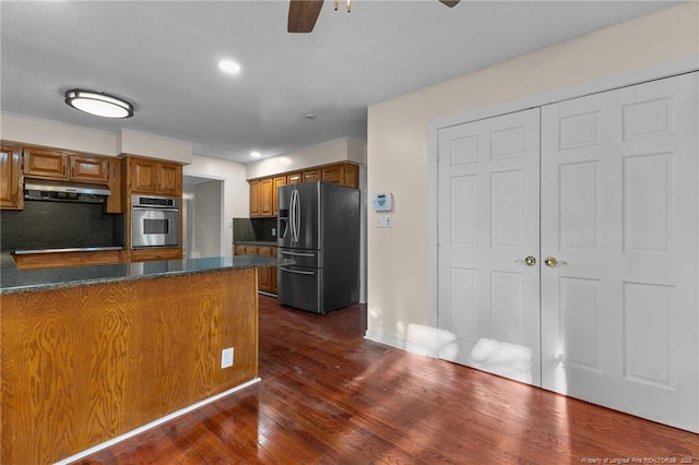 kitchen featuring brown cabinetry, dark wood-style floors, a peninsula, stainless steel appliances, and under cabinet range hood