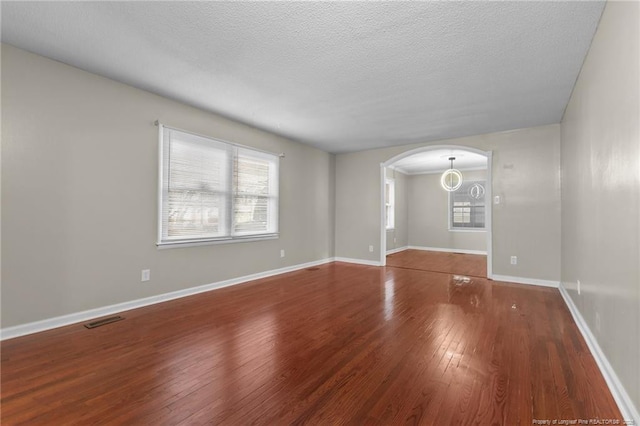 spare room with baseboards, visible vents, arched walkways, hardwood / wood-style flooring, and a textured ceiling