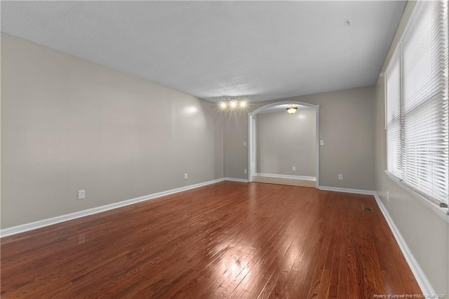 spare room with arched walkways, visible vents, baseboards, and wood finished floors
