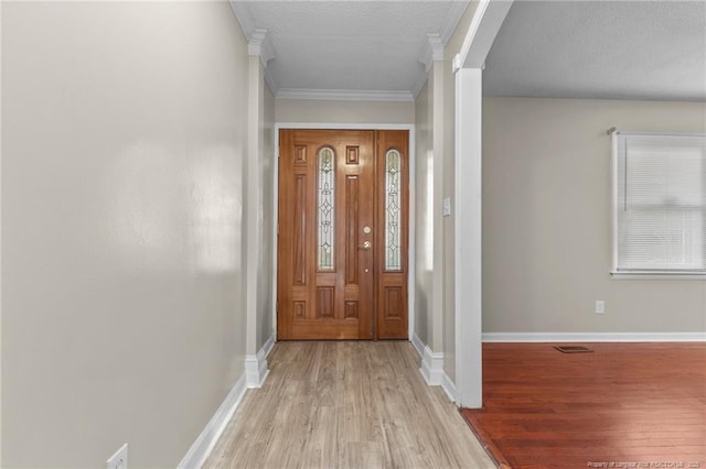 entryway with light wood-style floors, baseboards, crown molding, and ornate columns