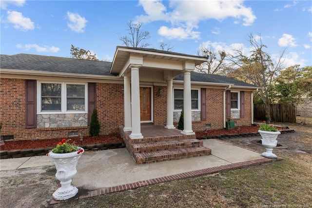view of exterior entry featuring crawl space, roof with shingles, fence, and brick siding