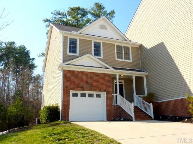 traditional home featuring covered porch, driveway, brick siding, and an attached garage