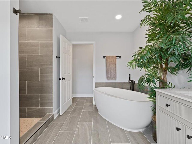 full bathroom featuring visible vents, baseboards, a freestanding tub, vanity, and tiled shower