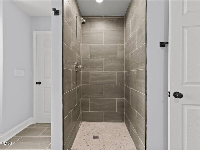 full bath with a tile shower, tile patterned flooring, and baseboards