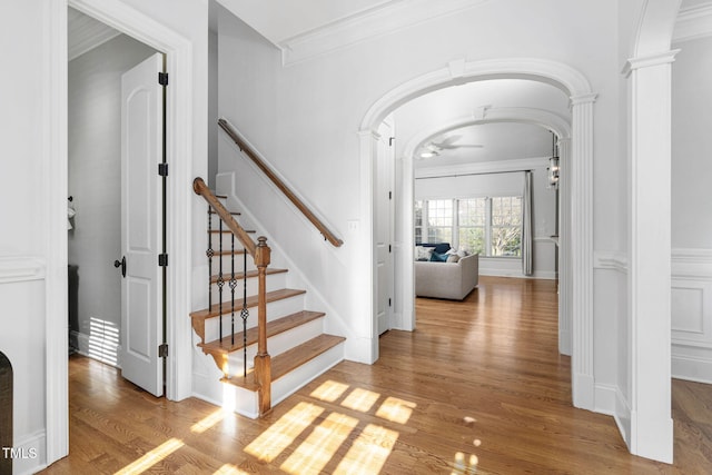 entrance foyer featuring crown molding, ornate columns, wood finished floors, a ceiling fan, and arched walkways