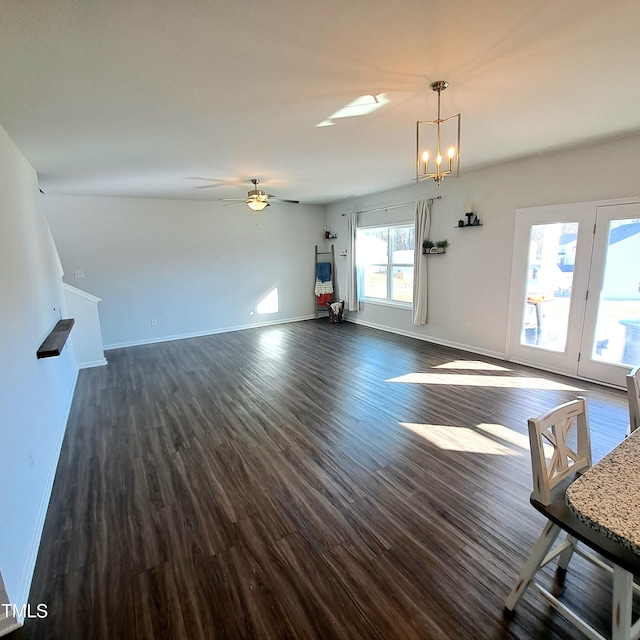 unfurnished living room with ceiling fan with notable chandelier, dark wood finished floors, and baseboards