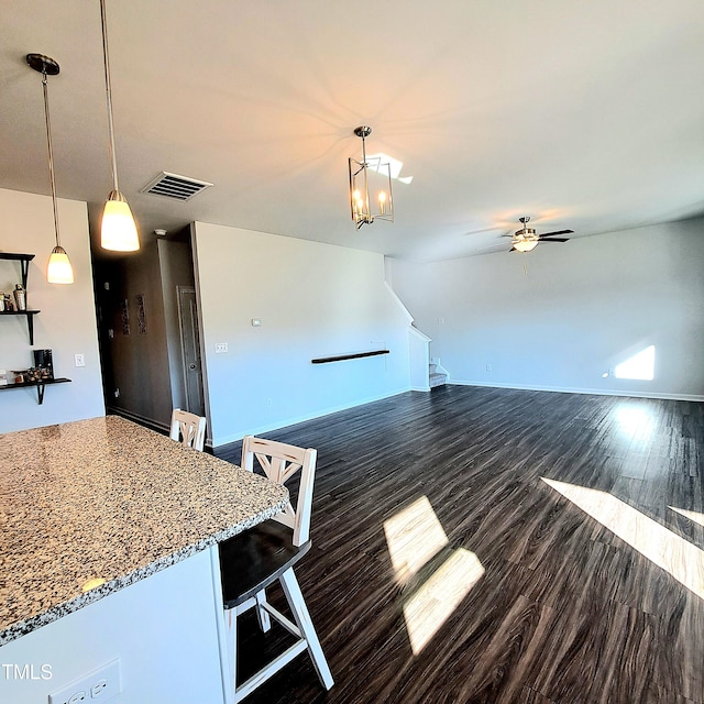 unfurnished living room featuring dark wood-style floors, visible vents, baseboards, and ceiling fan with notable chandelier