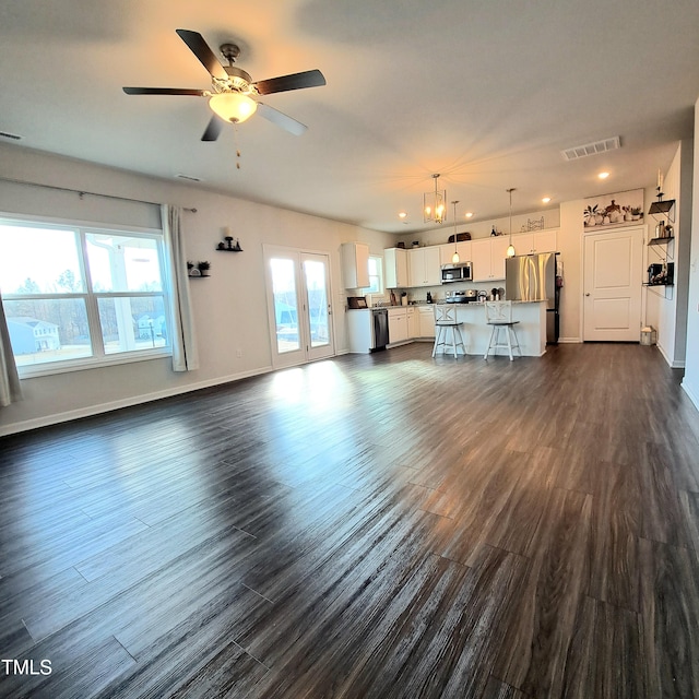 unfurnished living room with a ceiling fan, visible vents, dark wood finished floors, and baseboards