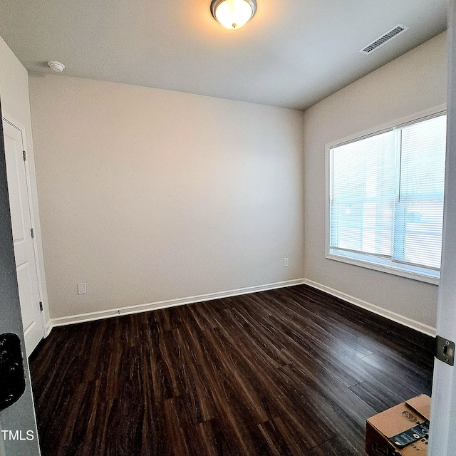 unfurnished room with visible vents, dark wood finished floors, and baseboards