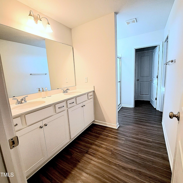 bathroom with double vanity, baseboards, visible vents, wood finished floors, and a sink