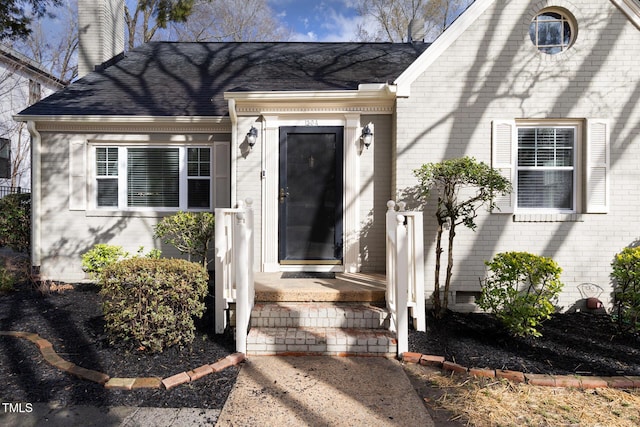 doorway to property featuring a shingled roof, brick siding, and a chimney