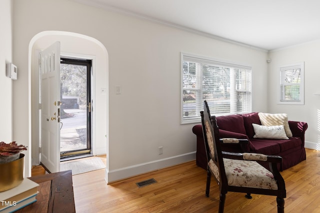 interior space with arched walkways, visible vents, ornamental molding, light wood-type flooring, and baseboards