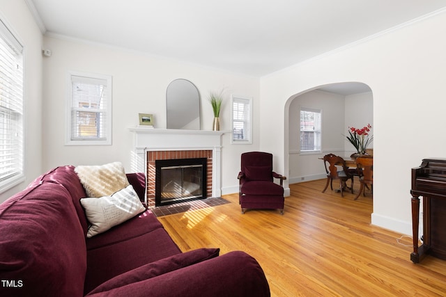 living area with ornamental molding, arched walkways, a brick fireplace, and light wood finished floors