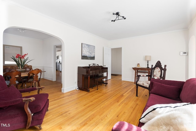 living room with arched walkways, light wood finished floors, baseboards, and crown molding