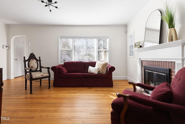 living room with a brick fireplace, crown molding, arched walkways, and light wood-style floors