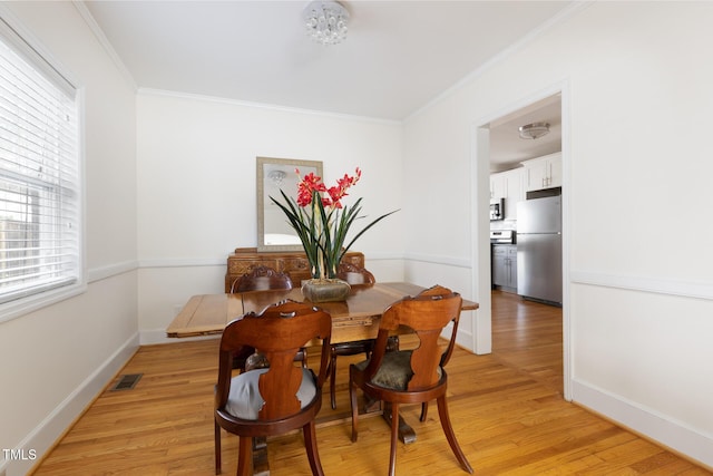 dining area featuring baseboards, light wood-style flooring, visible vents, and crown molding