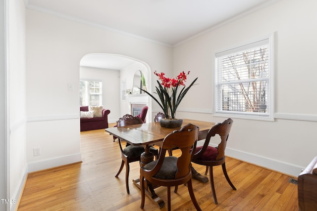 dining space featuring light wood finished floors, baseboards, arched walkways, and crown molding