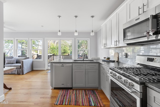 kitchen with dark countertops, a peninsula, stainless steel appliances, gray cabinetry, and a sink