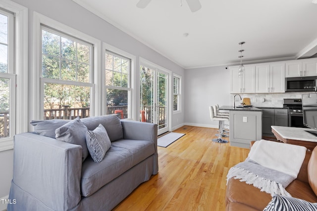 living room featuring ornamental molding, baseboards, light wood finished floors, and a ceiling fan