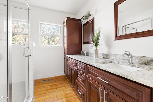 full bathroom with double vanity, visible vents, wood finished floors, a shower stall, and a sink