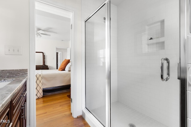 ensuite bathroom with ensuite bathroom, wood finished floors, vanity, a ceiling fan, and a stall shower