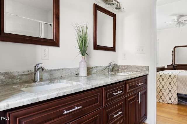 bathroom featuring a ceiling fan, wood finished floors, a sink, and double vanity