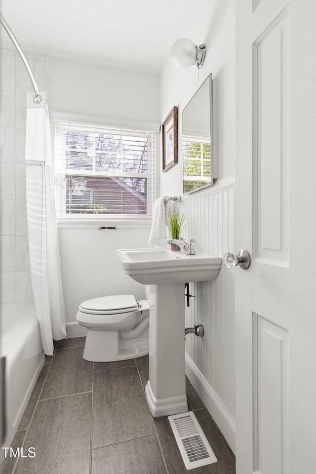 full bath featuring toilet, wainscoting, visible vents, and shower / tub combo with curtain