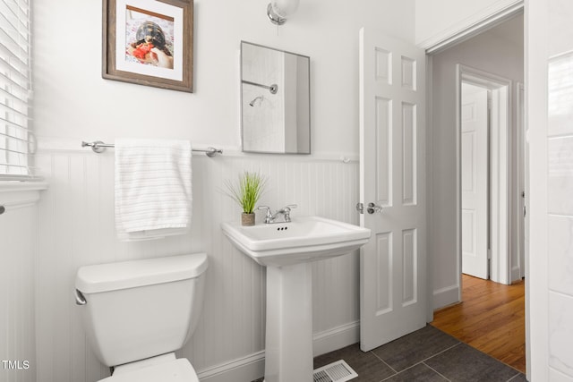 bathroom featuring a wainscoted wall, visible vents, toilet, a sink, and tile patterned flooring