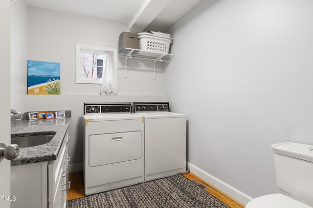 laundry room with laundry area, baseboards, light wood-style floors, washing machine and dryer, and a sink