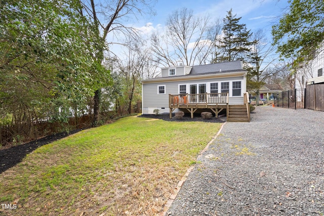 back of property featuring a wooden deck, crawl space, gravel driveway, fence, and a yard